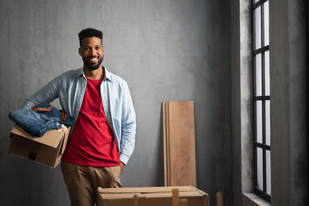 Happy young man holding packing boxes moving home, looking at camera, new living concept.の写真素材