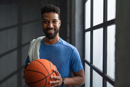 Happy young African American basketball player standing indoors at gym, looking at camera.の写真素材