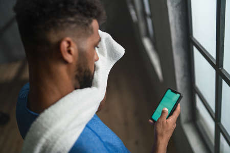 High angle view of young African American sportsman standing indoors at gym, using smartphone.の写真素材