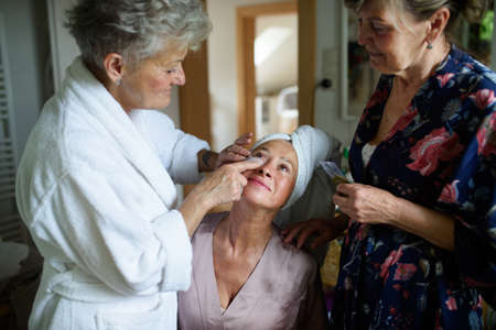 Happy senior women friends in bathrobes applying anti wrinkle patches indoors at home, selfcare concept.の写真素材