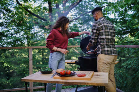 Happy biracial couple resting and preparing burgers outdoors in a tree house, weekend away and digital detox concept.の写真素材