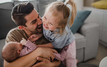 Happy young man taking care of his newborn baby and little daughter indoors at home, paternity leave.の写真素材
