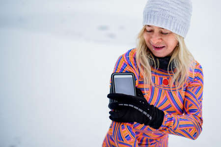 Active senior woman runner adjusting smartphone, attached to arm, for exercising outdoors in snowy...