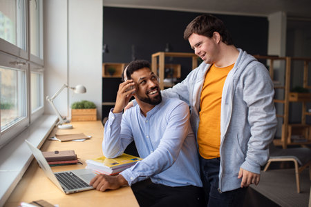 Happy young man with Down syndrome and his tutor using lapotp indoors at school.の写真素材