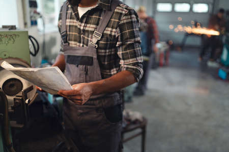 Close up of young industrial man holding blueprints indoors in metal workshop.の写真素材