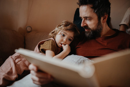Mature father with small daughter resting indoors at home, looking at photo album.