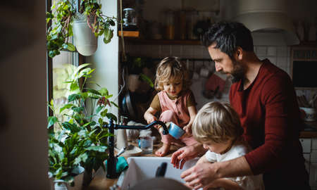 Mature father with two small children washing dishes indoors at home, daily chores concept.の写真素材