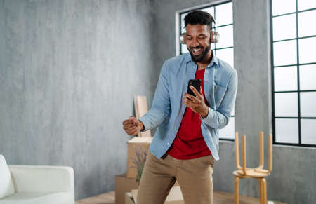 Happy young man with headphones dancing and celebrating moving home surrounded by packing boxes