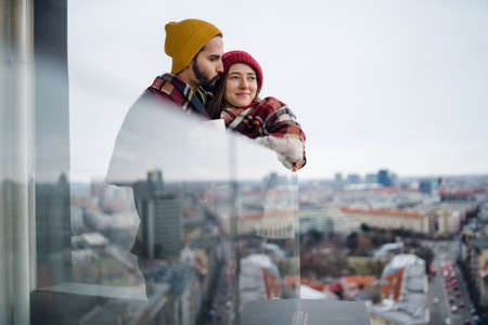 Young couple wrapped in blanket standing and hugging outdoors on balcony, shot through glass.の写真素材