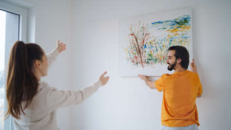 Young couple arranging new flat, hanging up painting, new home and relocation concept.の写真素材