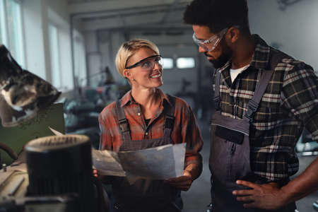 Portrait of young biracial industrial colleagues working indoors in metal workshop, smiling.
