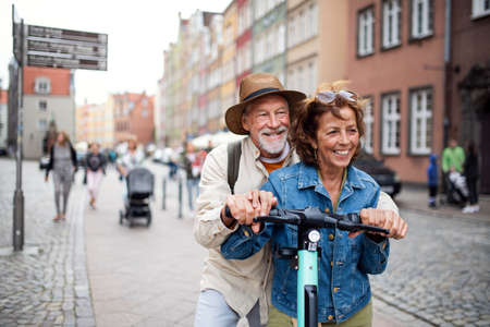 Portrait of happy senior couple tourists riding scooter together outdoors in townの写真素材