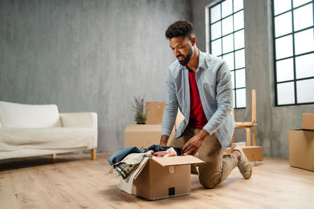 Happy young man putting clothes into packing boxes, moving home. New living concept.の写真素材