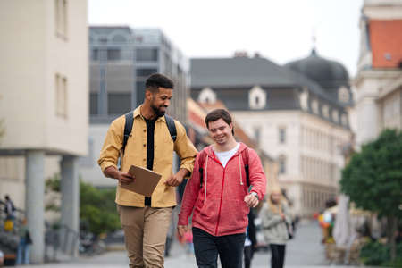 Young man with Down syndrome and his mentoring friend walking and talking outdoorsの写真素材