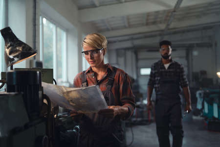 Portrait of young biracial industrial colleagues working indoors in metal workshop, smiling.の写真素材