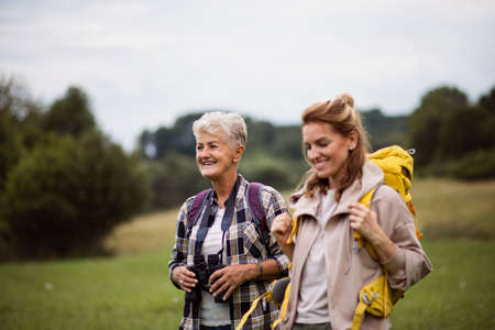 Active senior woman with binoculars hiking with her adult daughter outdoors in nature.の写真素材