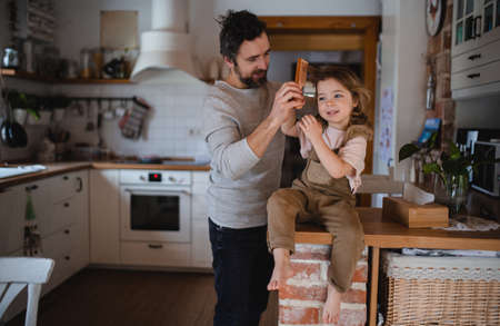 Mature father with small daugther resting indoors at home and combing hair.の写真素材