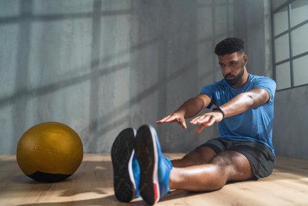 Young sportsman sitting on floor and doing stretching exercise indoors, workout training concept.