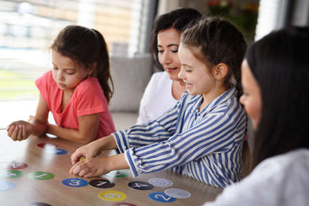 Happy small girls with mother and grandmother playing cards indoors at home.の写真素材
