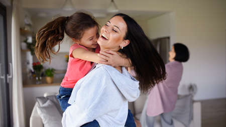 Happy small girl with mother indoors at home, having fun, hugging.