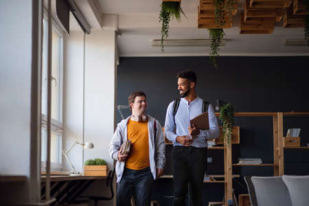 Young man with Down syndrome and his tutor looking at each other indoors at schoolの写真素材