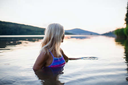 Side view of active senior woman swimmer diving outdoors in lake.の写真素材