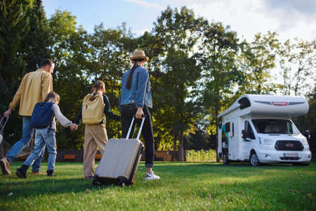 Rear view of young family with suitcases going to caravan outdoors at park.の写真素材