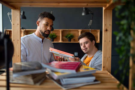 Young happy man with Down syndrome and his tutor indoors at staffroom.の写真素材