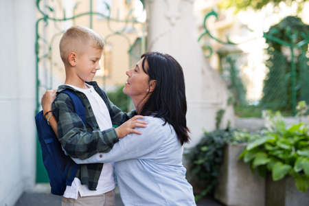 Happy schoolboy hugging his grandmother waiting for him after school outdoors in street.の写真素材