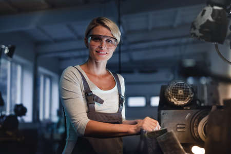 Portrait of mid adult industrial woman working indoors in metal workshop, looking at camera.