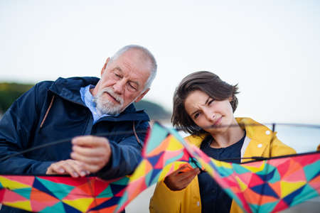 Senior man and his preteen granddaughter preparing kite for flying on sandy beach.の写真素材