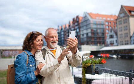 Portrait of happy senior couple tourists doing selfie outdoors in historic townの写真素材