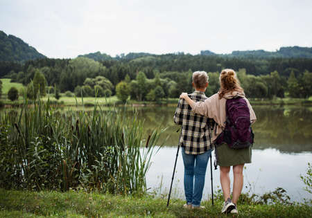 Rear view of senior mother embracing with adult daughter when standing by lake outdoors in natureの写真素材