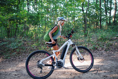 Active senior woman biker pushing ebike outdoors in forest.の写真素材