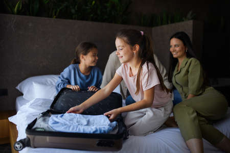 Happy young family with two children sitting on bed and unpacking at luxury hotel, summer holiday.の写真素材