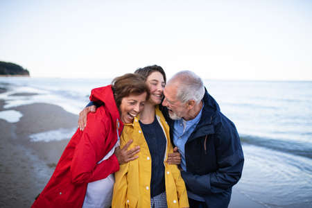 Senior couple and their preteen granddaughter hugging when walking on sandy beach.の写真素材