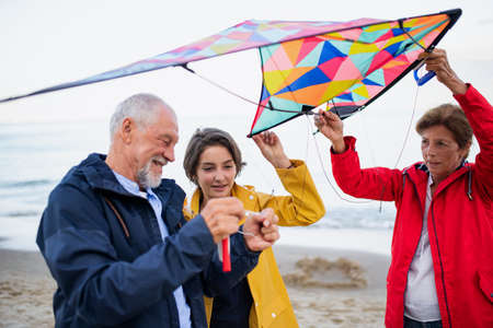 Grandparents with preteen girl preparing kite for flying on sandy beach.の写真素材