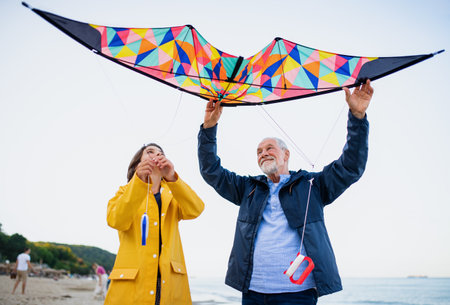 Low angle view of preteen girl and her grandfather playing with kite on sandy beach.の写真素材