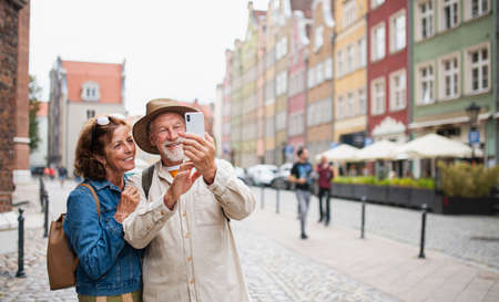Portrait of happy senior couple tourists making selfie outdoors in historic townの写真素材