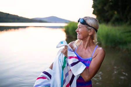 Portrait of active senior woman swimmerdrying herself with towell outdoors by lake.の写真素材