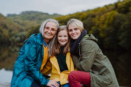 Portrait of small girl with mother and grandmother sitting and looking at camera outoors in nature.の写真素材