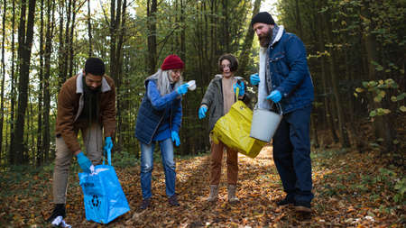 Diverse group of happy volunteers cleaning up forest from waste, community service concept.
