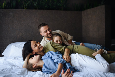 Happy young family with two children lying on bed at hotel, summer holiday.の写真素材