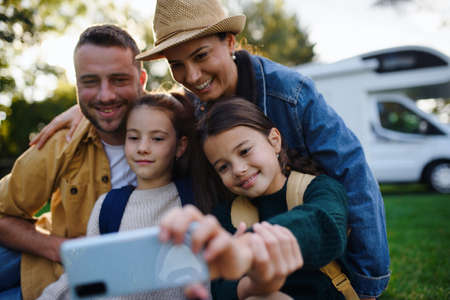 Happy young family with two children ltaking selfie with caravan at background outdoors.の写真素材