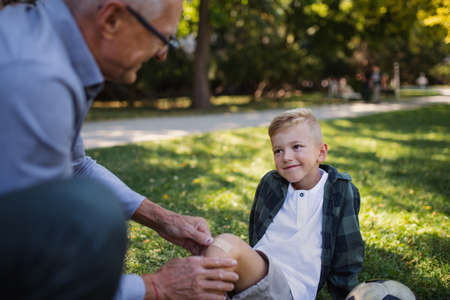 Little boy with injured leg getting plaster from grandfather outdoors in park.の写真素材