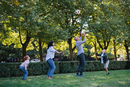 Happy little children with grandparents playing with football outdoors in parkの写真素材