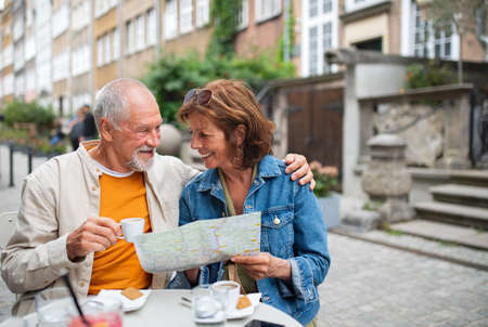 Portrait of happy senior couple tourists sitting and using map outdoors in town.