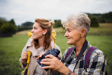 Happy senior mother hiker with adult daughter holding binoculars outdoors in natureの写真素材