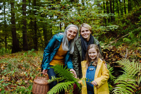 Small girl with mother and grandmother on walk outoors in forest, looking at camera.の写真素材