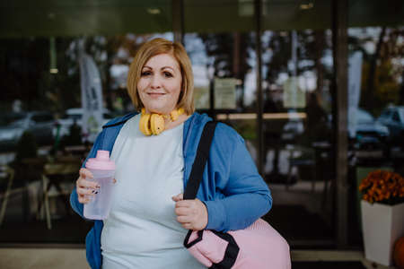 Happy overweight woman in sports clothes looking at camera outdoors in front of fitness centerの写真素材